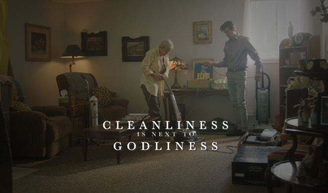 text cleanliness is next to godliness, a woman speaks with a man holding a vacuum